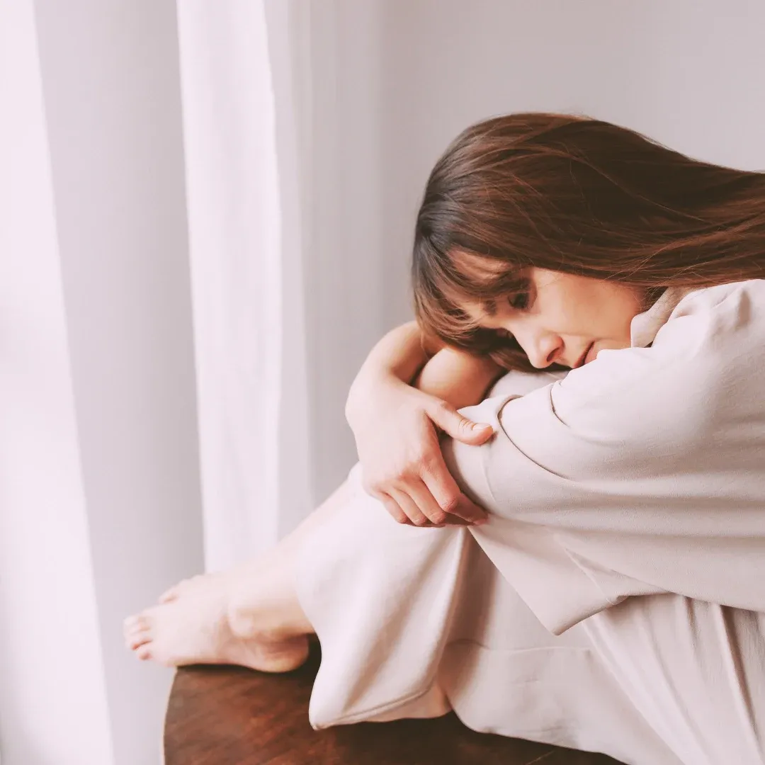 Une personne assise près d’une fenêtre, plongée dans ses pensées